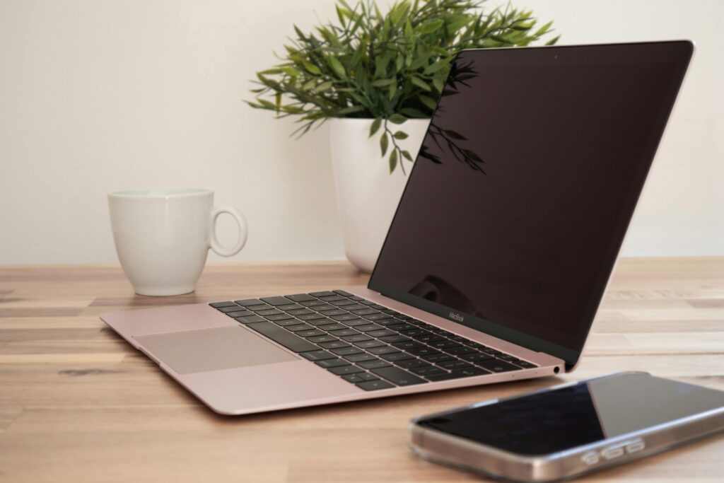 A stylish workspace featuring a rose gold laptop, coffee mug, and plant on a light wooden desk.